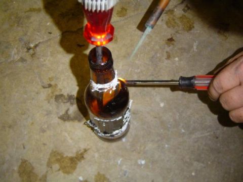 1979 Ford Bronco - A person is modifying a glass bottle using heat from a soldering iron and a screwdriver.