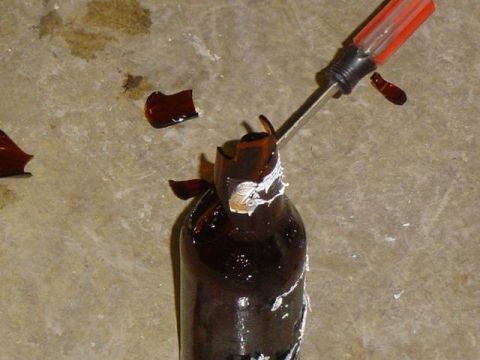 1979 Ford Bronco - A screwdriver is used to break a brown bottle on a concrete surface.