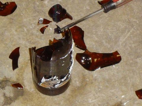 1979 Ford Bronco - A screwdriver is used to break apart a shattered brown glass bottle on a concrete surface.