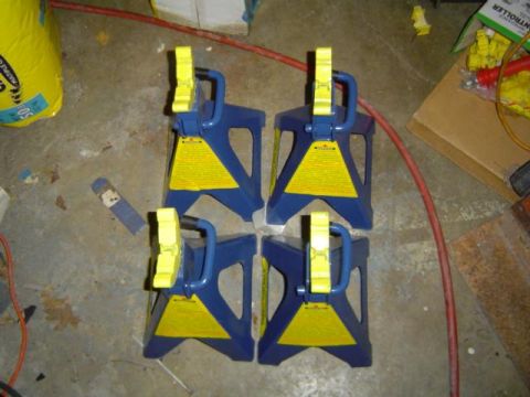 1979 Ford Bronco - Four jack stands are arranged on a concrete floor, with a yellow bag and some debris in the background.