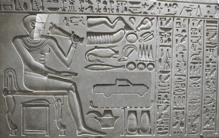 Ancient Egyptian relief carving depicting hieroglyphs, a seated figure, animals, and a pickup truck