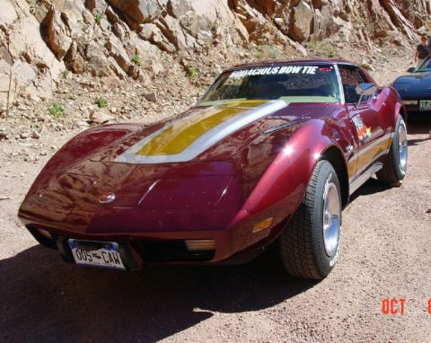 1972 Ford Ranchero - A maroon 1975 Chevrolet Corvette with distinctive hood stripes is parked on a gravel road, with another vehicle visible behind it.