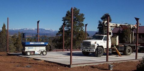 1986 Ford Ranger - A white utility truck with a crane is parked next to a blue scissor lift on a concrete pad with mountains in the background.
