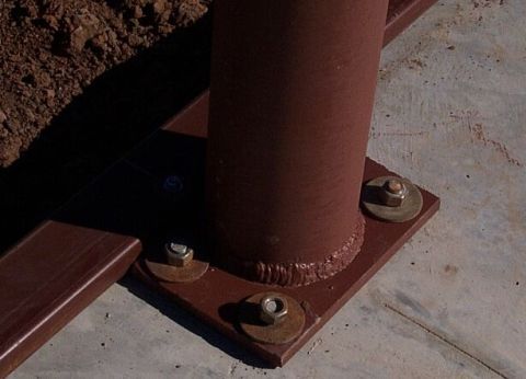 1986 Ford Ranger - Close-up of a metal pole's base, secured with bolts to a concrete surface. A dirt pile is visible to the left.