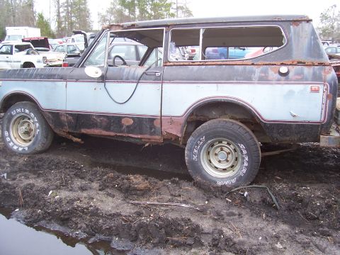 1978 Ford Bronco - This heavily rusted International Scout II sits in a muddy junkyard with other vehicles visible.