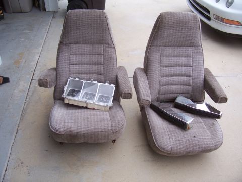 1978 Ford Bronco - Two fabric car seats are displayed with a dashboard instrument cluster and chrome trim pieces, suggesting they are parts from a vehicle.