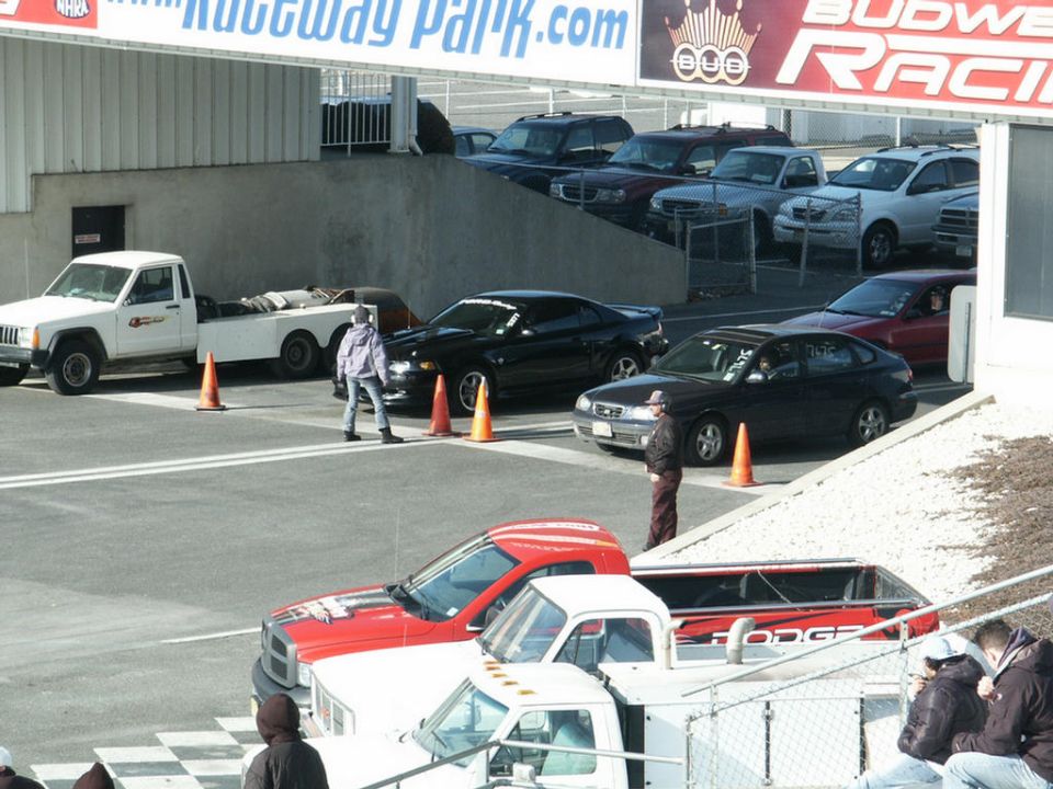 Cars lined up in drag strip staging lanes with cones and officials under Raceway Park banners