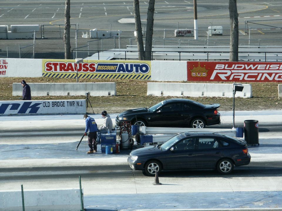Dark sedan and black coupe on a race track, with people preparing for a race