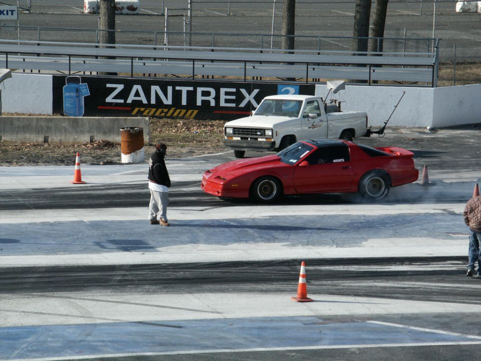 Red sports car with black roof on racetrack, white pickup truck behind