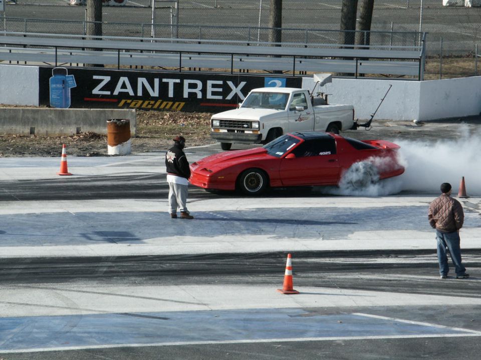 Red third-gen Pontiac Firebird doing a smoky burnout at a drag strip