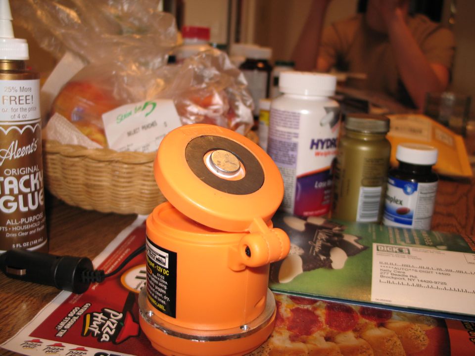 Orange magnetic light with a car adapter and various bottles and a basket of fruit on a table