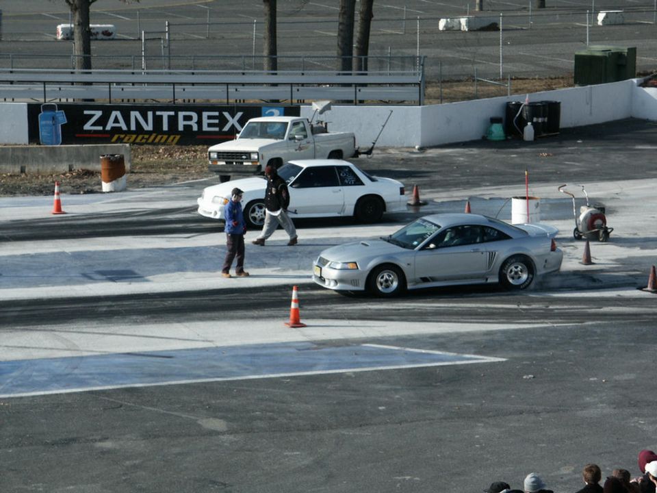 Silver New Edge Mustang staging at a drag strip with a white Fox-body Mustang and pickup behind
