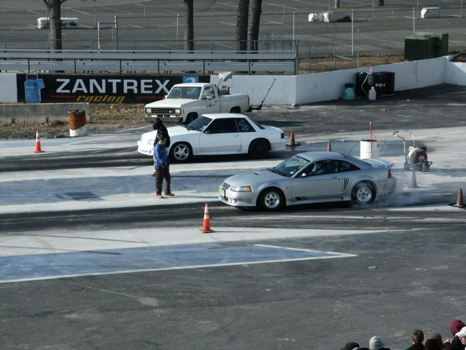 Silver coupe with racing modifications, side view, emitting smoke from rear tires