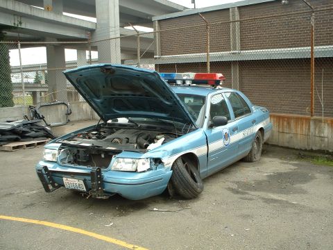 1999 Ford Crown Victoria - This damaged 1999 Ford Crown Victoria police car sits with its hood open and flat tires, possibly after an incident.