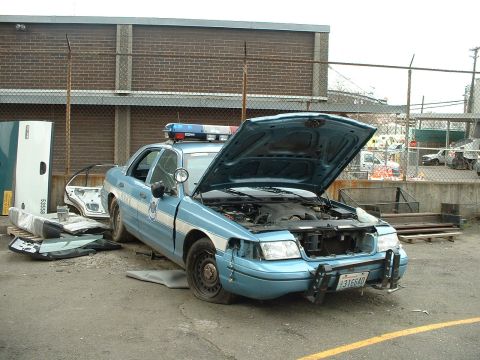 1999 Ford Crown Victoria - This police car appears to be undergoing repairs or is being dismantled, with its hood up and parts laid out.