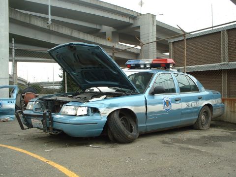 1999 Ford Crown Victoria - A damaged Seattle police car sits with its hood open and flat tires, showing signs of significant wear and tear.