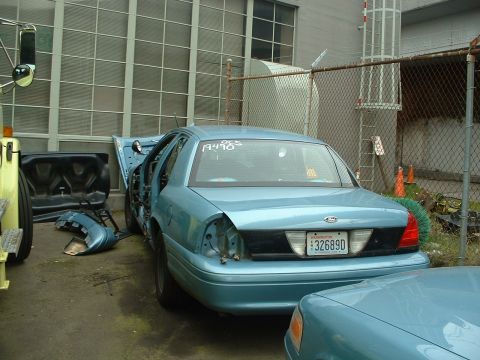 1999 Ford Crown Victoria - This light blue Ford Crown Victoria appears to be undergoing repairs or dismantling, with its doors ajar and several parts removed.