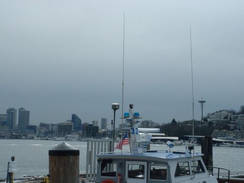 1999 Ford Crown Victoria - A boat with antennas is docked in Seattle harbor, with the city skyline and Space Needle in the distance.