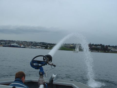 1999 Ford Crown Victoria - A boat equipped with a water cannon operates on the water, with a distant sailboat and city visible.