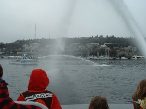 1999 Ford Crown Victoria - A police boat sprays water in a harbor, with people in the foreground watching.
