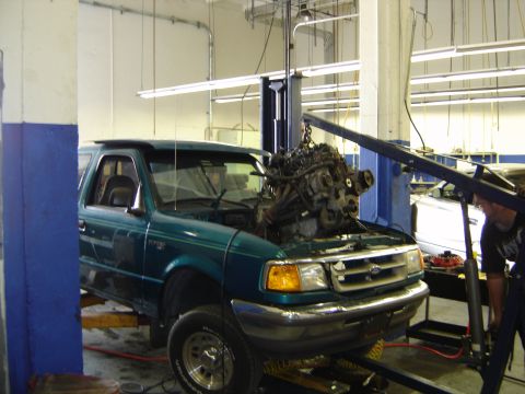 1997 Ford Ranger - A mechanic is removing the engine from a green Ford Ranger that is on a lift.