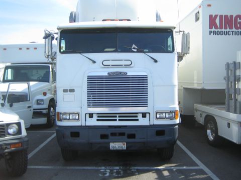 1990 Ford Bronco - white Freightliner cabover semi-tractor is parked head-on in a lot among box trucks, wearing California plate 9A43087.