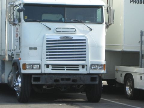 1990 Ford Bronco - white Freightliner cabover semi-tractor photographed head-on, parked between box trailers in a lot.