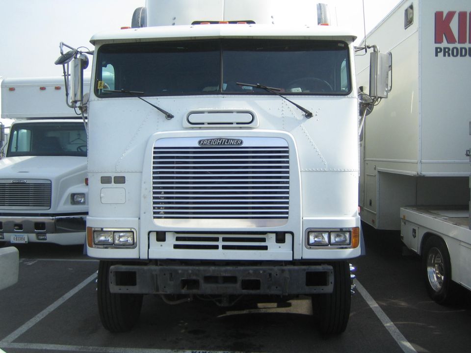 White Freightliner cabover semi tractor front view in a lot among box trucks
