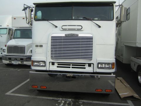 1990 Ford Bronco - white Freightliner cabover semi-tractor with a chrome step bumper and amber marker lights, photographed head-on in a parking lot.