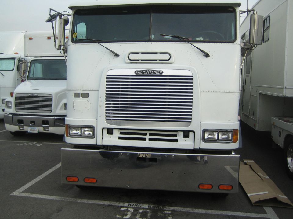 White Freightliner cabover semi with chrome bumper and amber lights, front view