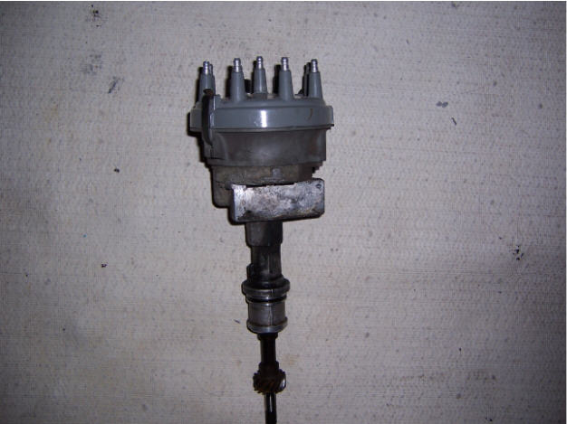 Ford V8 distributor with gray cap and gear shaft laid on carpet