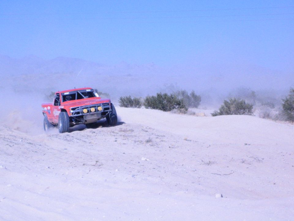Red off-road race truck kicking up dust on a desert course