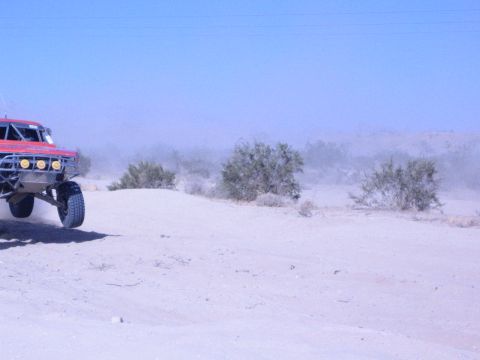 Red off-road race truck at the edge of a dusty desert race course