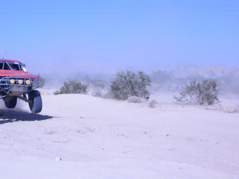 Red off-road race truck at the edge of a dusty desert race course