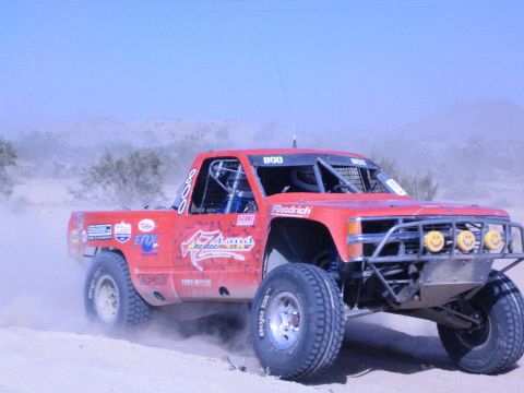 Red number 800 off-road race truck cornering hard in the desert dirt