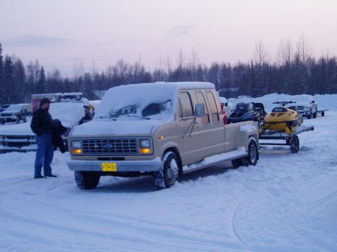 2000 Ford E350 - 3/4-front view of a tan Ford Econoline van converted into a crew-cab dually pickup, snow piled on its roof and hood, parked on a snowy lot…