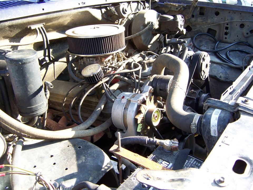 Engine bay with carburetor, air filter, alternator, and battery visible
