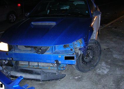 2000 Ford Crown Victoria - A blue car with significant front-end damage is viewed from the front, revealing exposed mechanical components.
