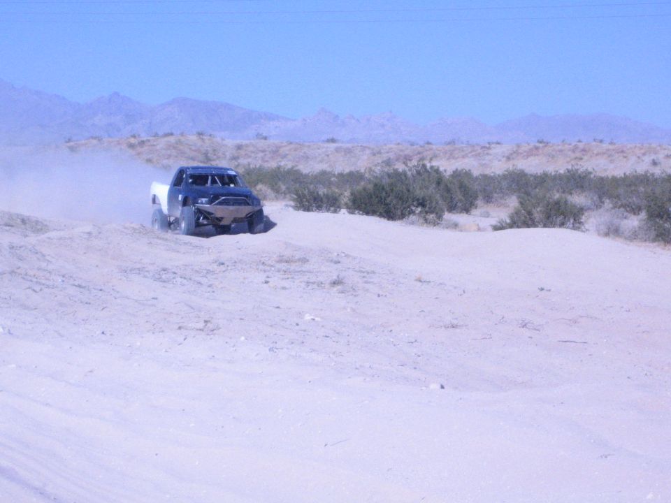 Dark-cab off-road race truck on a sandy desert trail near mountains
