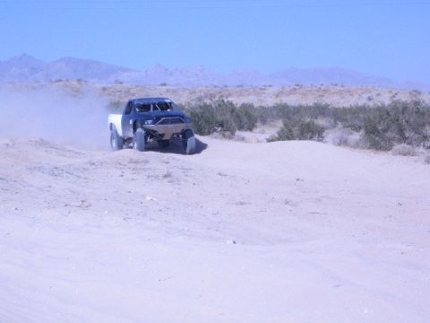 Off-road race truck with white bed cresting a desert berm