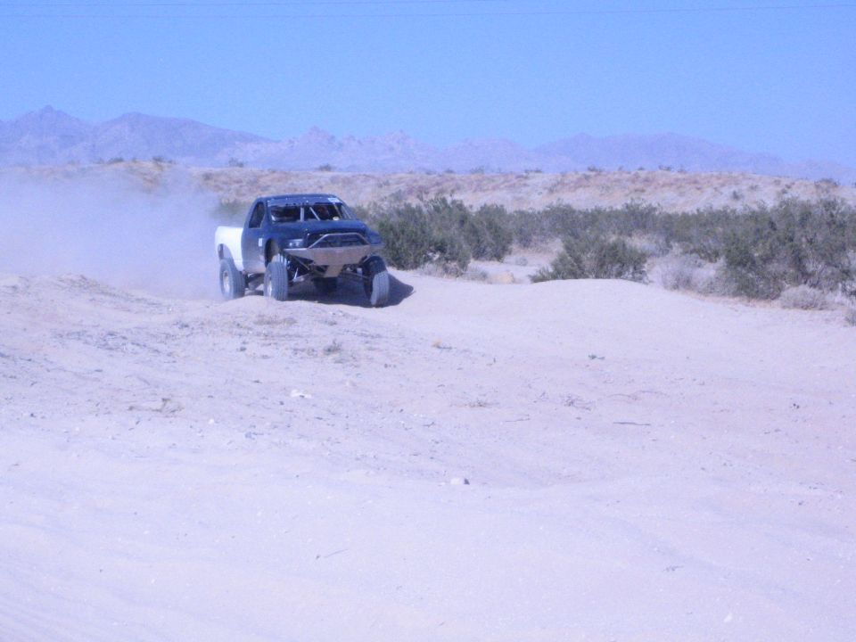 Off-road race truck with white bed cresting a desert berm