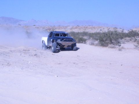 Off-road race truck with white bed on a desert course near mountains