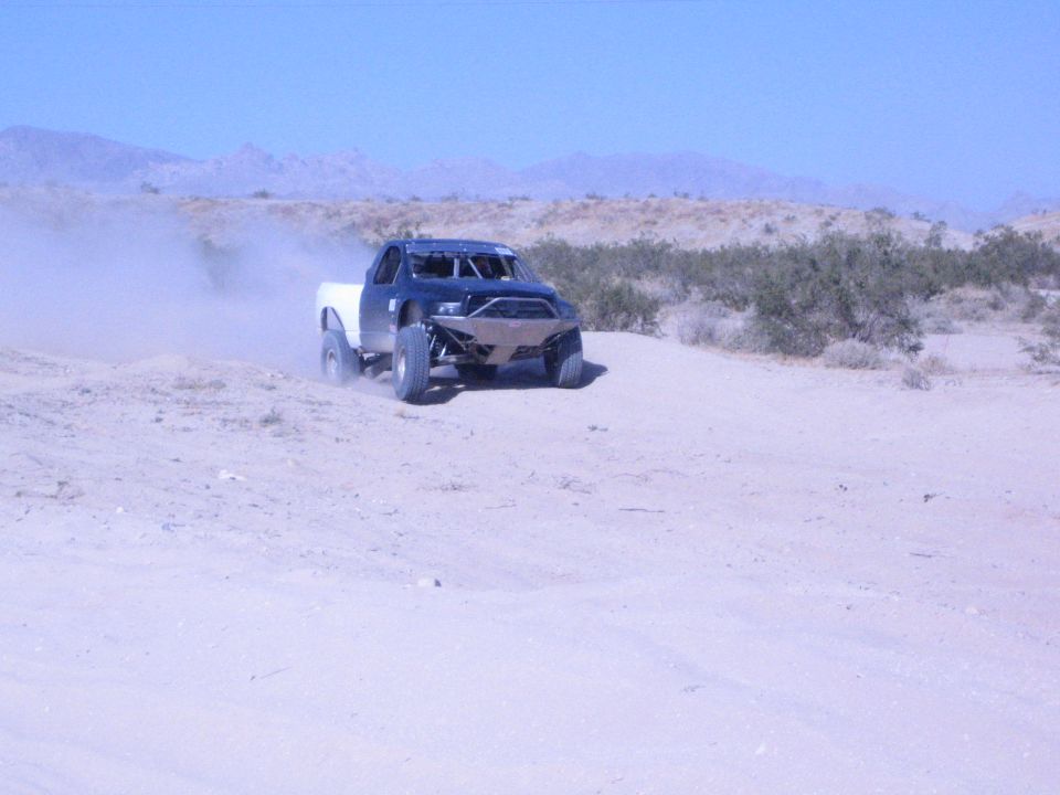 Off-road race truck with white bed on a desert course near mountains