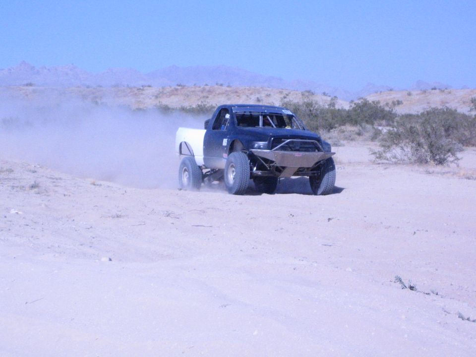 Off-road race truck with white bed crossing desert sand at speed