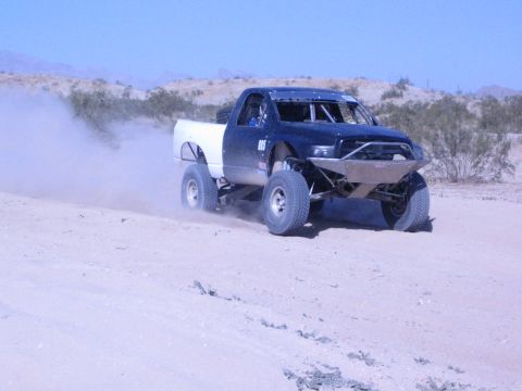 Off-road race truck with white bed cornering on a desert course