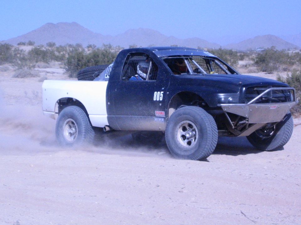 Black off-road race truck number 805 with white bed in the desert