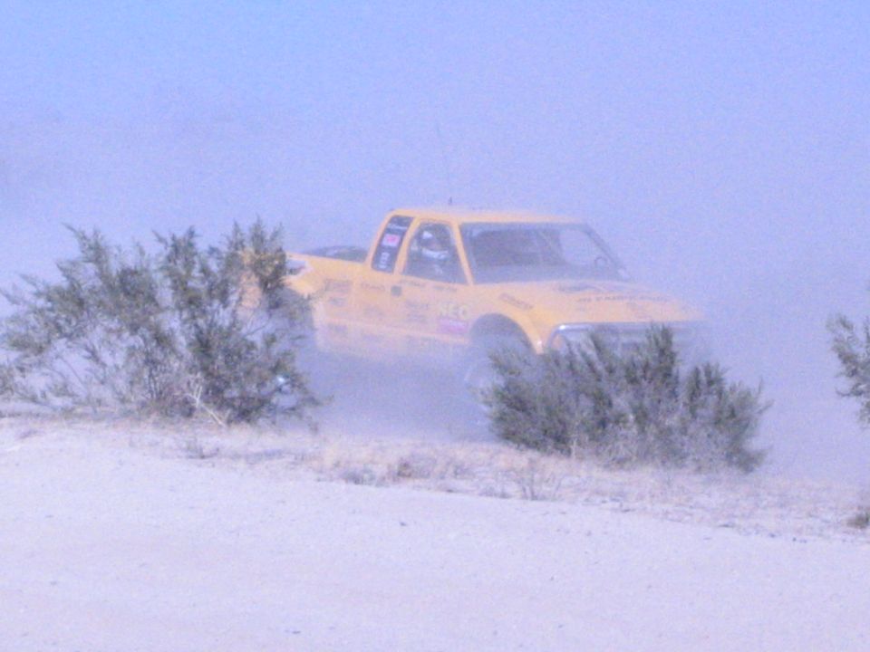 Yellow off-road race truck partly hidden by brush and dust in the desert