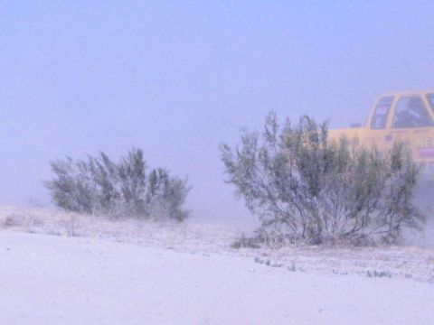 Yellow truck barely visible behind desert brush in heavy dust