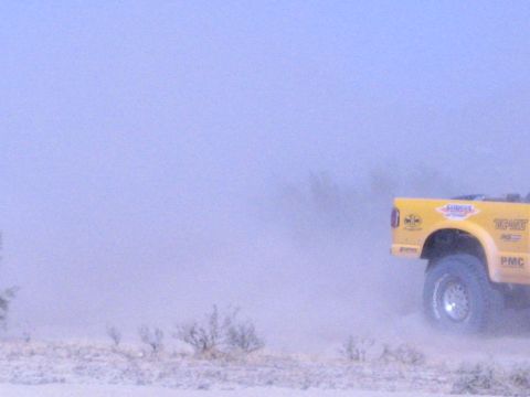 Rear of a yellow off-road race truck speeding away through desert dust