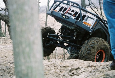 1995 Ford Bronco - A heavily modified off-road vehicle navigates challenging rocky terrain with a person in blue jeans visible on the right.